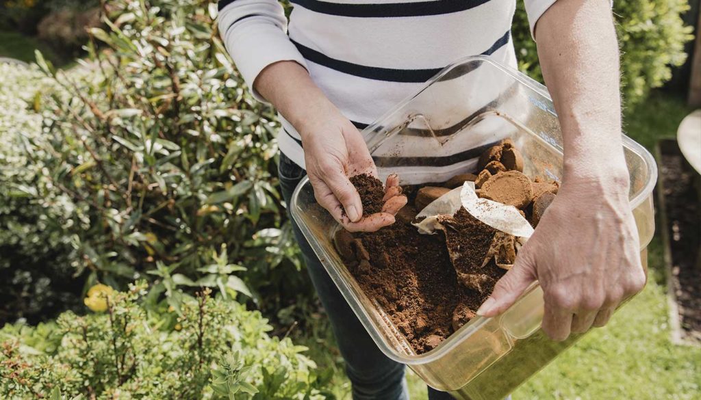 Person holding a tub of used coffee grounds