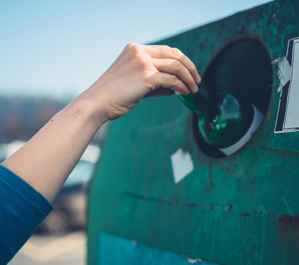 Person dropping glass bottle into bottle bank