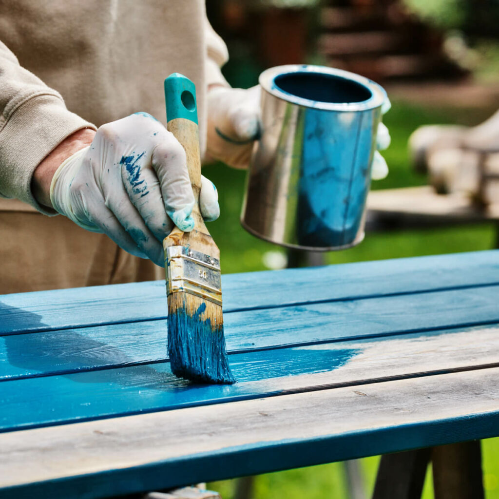 Person painting bench with blue paint